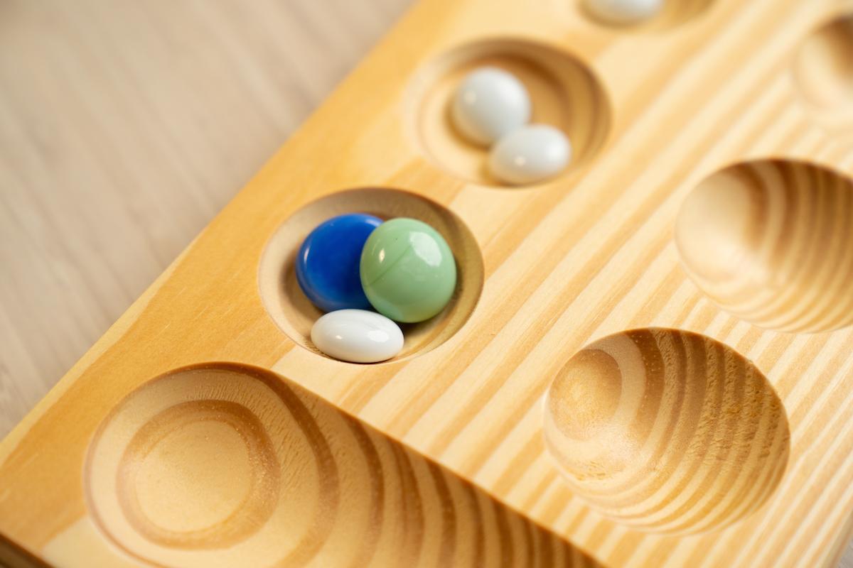 Glass stones sitting in pits on a mancala board
